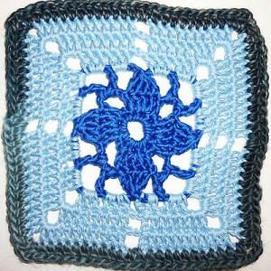 Quadratisches, handgehäkeltes Granny Square in Blautönen mit zentralem Blütenmotiv