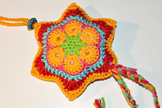Bunter gehäkelter Stern mit African‑Flower‑Zentrum, Aufhängeschlaufe, Perle und geflochtenen Bändern