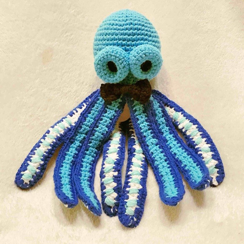 Gehäkelter Oktopus-Amigurumi in Blau und Türkis mit großen Augen und brauner Fliege