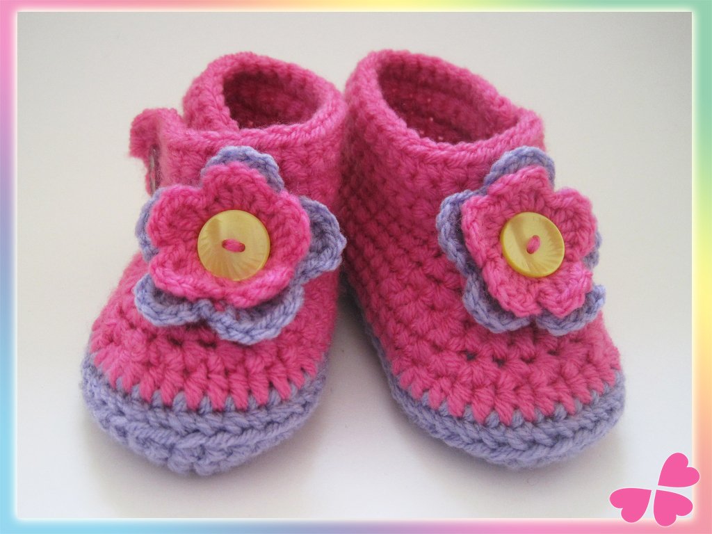 Nahaufnahme zweifarbiger gehäkelter Babyschuhe mit Blütenapplikation und Knopf