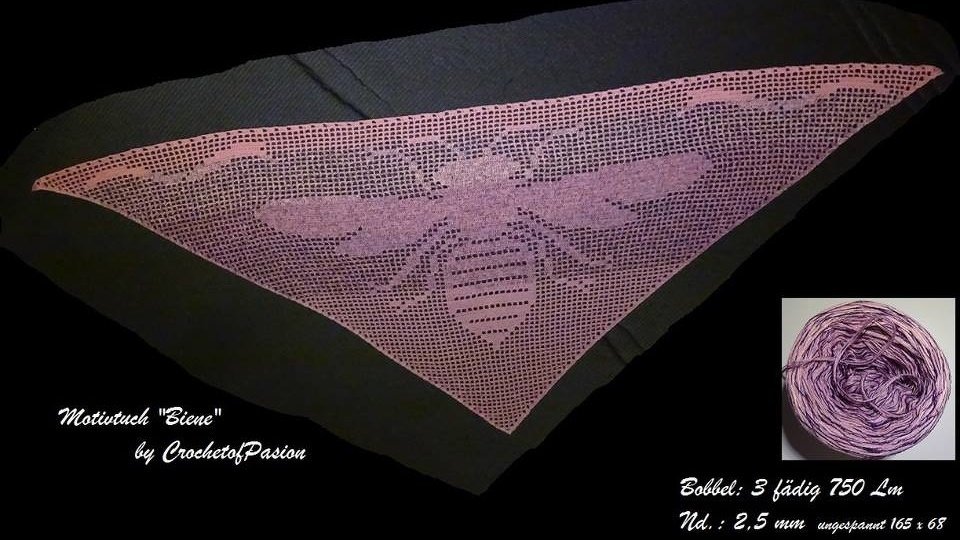 Dunkles Dreieckstuch, gehäkelt mit großem Bienenmotiv in Rosa‑Lila; daneben ein passendes Garnknäuel.