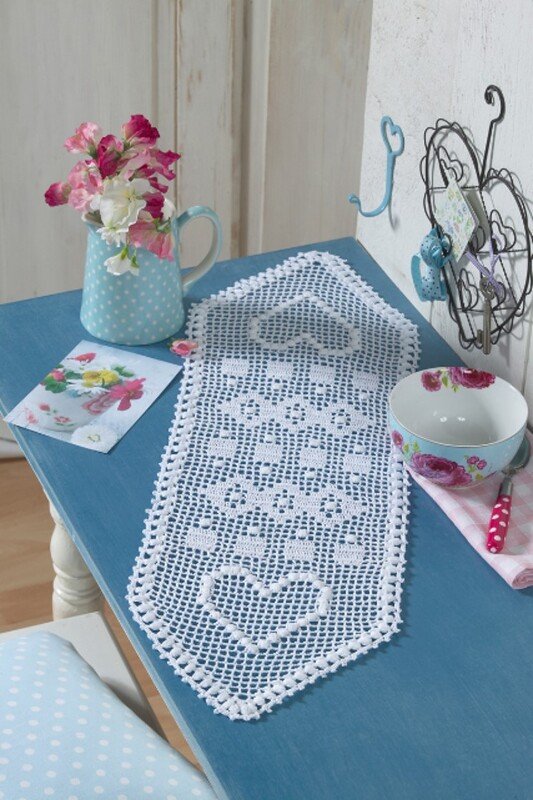 Romantischer weißer gehäkelter Läufer mit Herzmotiven auf blauem Tisch neben Blumen und Schale