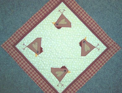 Quadratische Decke diagonal gelegt mit kariertem Rand und vier applizierten Vögeln