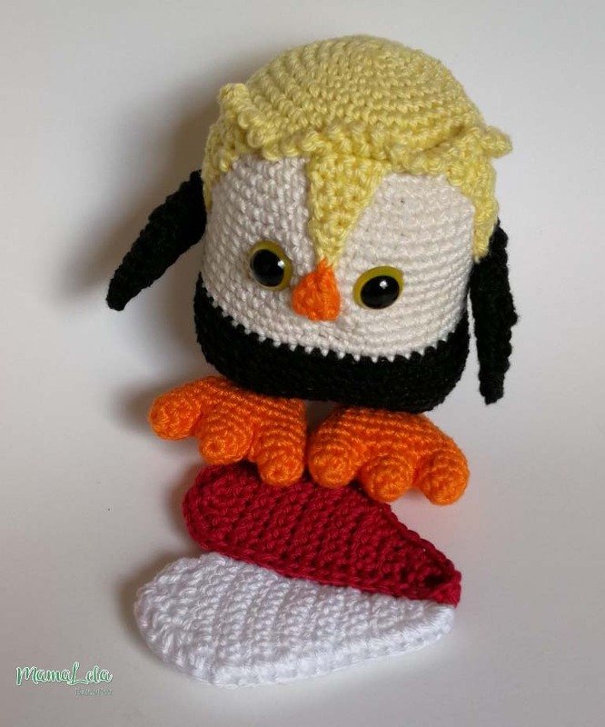 Gehäkelter Amigurumi-Pinguin mit gelber Haube und gehäkeltem Herz