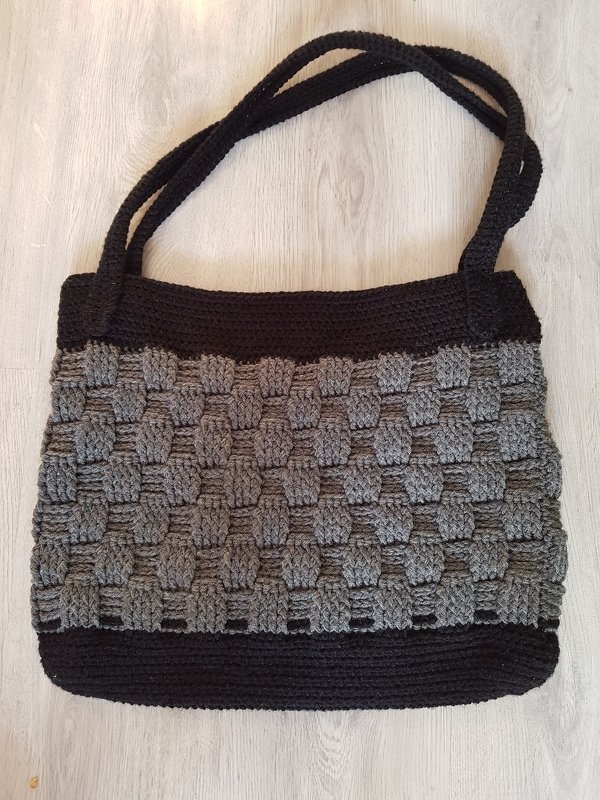 Gehäkelter schwarzer und grauer Shopper mit Korbmuster und langen Tragegurten auf hellem Boden