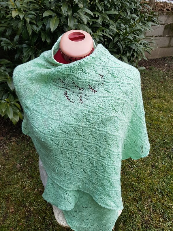 Light mint green knitted lace shawl with wavy lace pattern on a dress form