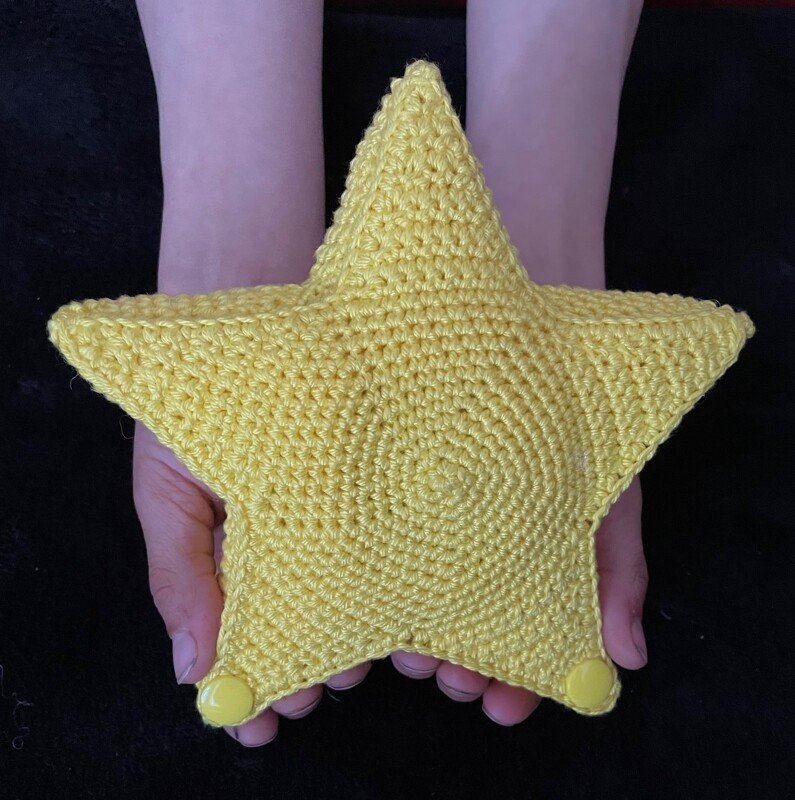 Gelbes gehäkeltes Sternkissen, in zwei Händen gehalten