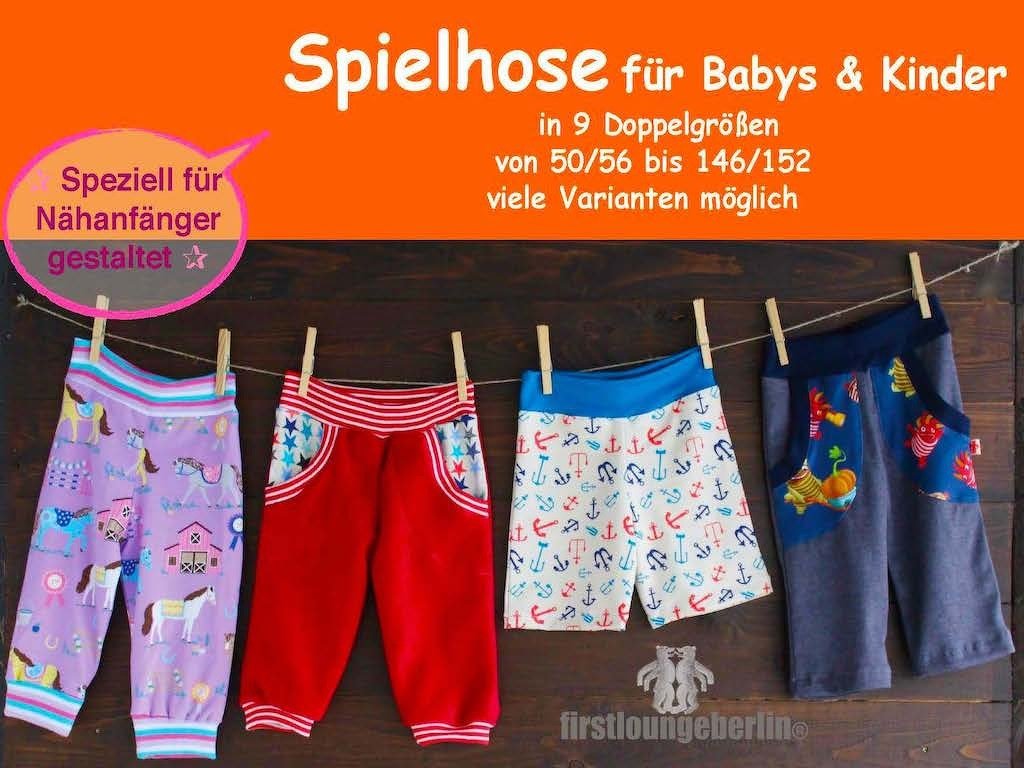 Vier farbige Kinderhosen (lila mit Pferden, rote Hose mit Sternen, weiße Shorts mit Ankern, blaue Hose mit Tiermotiven) an einer Wäscheleine vor einer Holzwand.