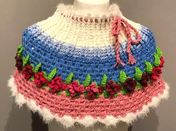 Gehäkelter Kragenschal mit 3D-Blumen, grünen Blättern und Farbstreifen in Blau, Rosa und Creme auf einer Büste.