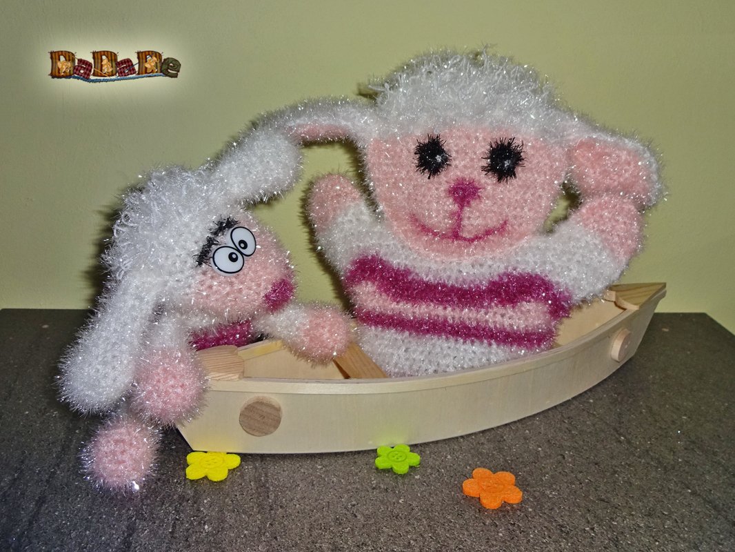 Zwei flauschige gehäkelte Lämmer in einem Holzboot, weiß und rosa gestreift