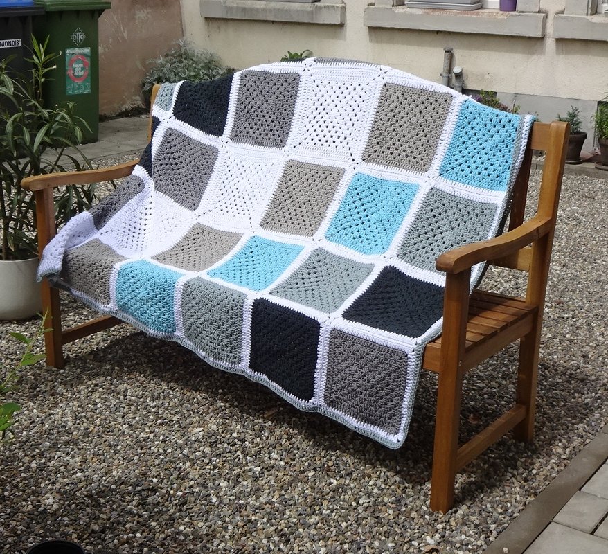 Gehäkelte Decke aus Granny Squares in Grau, Türkis und Weiß auf einer Holzbank