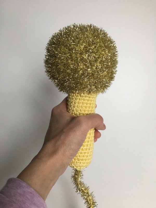 Gehäkelter gelber Griff mit rundem, goldglitzerndem Pompomkopf und Glitzerquaste.
