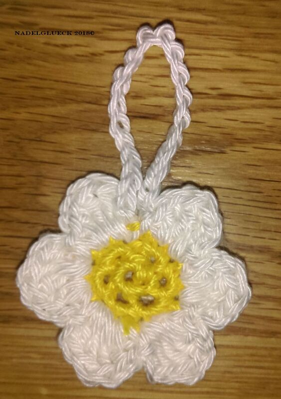 Gehäkelte weiße Margeritenblume mit gelbem Zentrum und Aufhängeschlaufe auf Holzuntergrund
