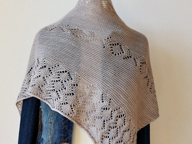 Taupe knitted lace shawl with leaf motifs draped over a mannequin wearing a denim jacket.