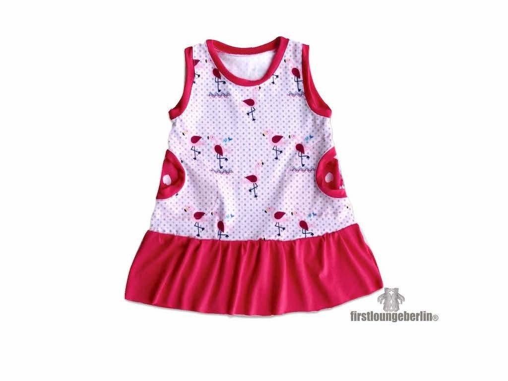 Ärmelloses Kinderkleid weiß mit Flamingo- und Punktmuster, runden rosa Seitentaschen und pinkem Rüschensaum