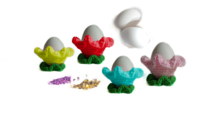 Gehäkelte bunte Eierbecher in Blumenform mit grünem Blattfuß und Eiern