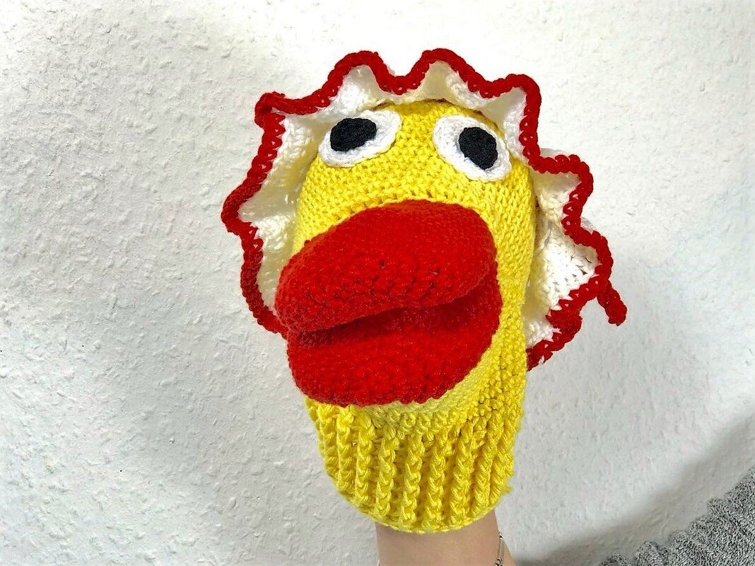 Gehäkelte gelbe Enten-Handpuppe mit großem roten Schnabel und weiß-rotem Rüschenrand