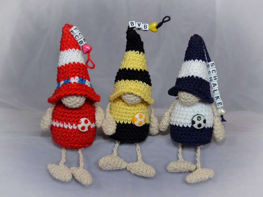 Drei gehäkelte Wichtel-Schlüsselanhänger in rot, gelb-schwarz und blau-weiß mit Buchstabenperlen und Fußballknöpfen