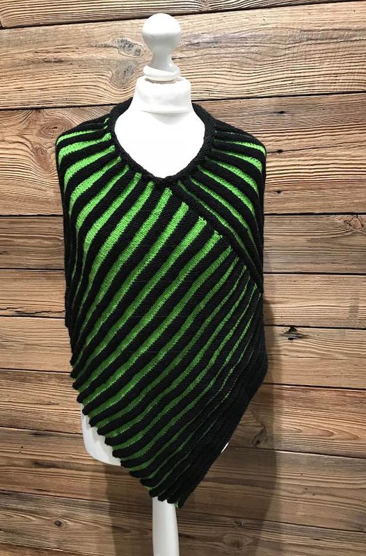 Asymmetrischer gestrickter Poncho in Schwarz und Grün auf Schaufensterpuppe vor Holzverkleidung
