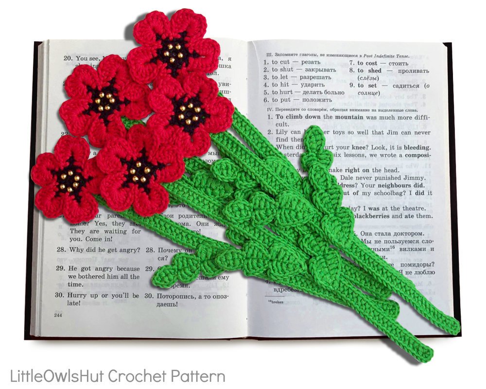 Close-up of floral crochet bookmarks with green leaf stems and beaded centers on an open book