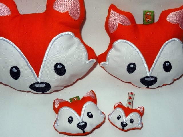 Vier gestickte Fuchsköpfe in verschiedenen Größen, orange und weiß, auf hellem Hintergrund.