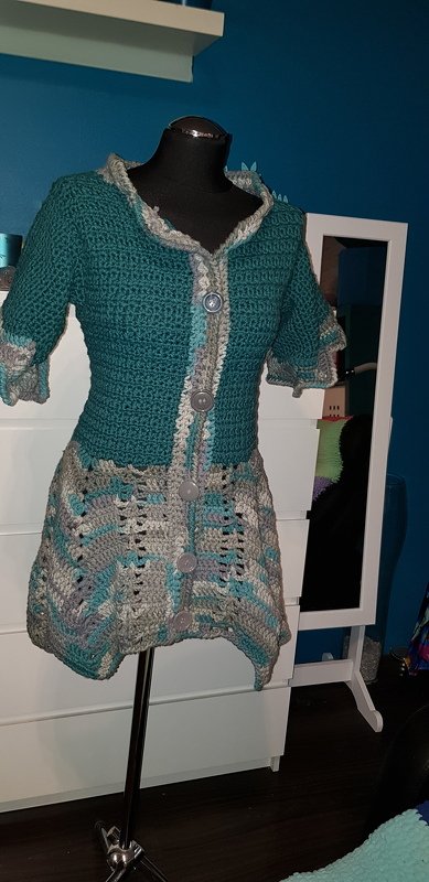 Gehäkelte Damenjacke in Petrol, Grau und Hellblau auf einer Schaufensterpuppe, kurze Ärmel, Wellenmuster und Knöpfe