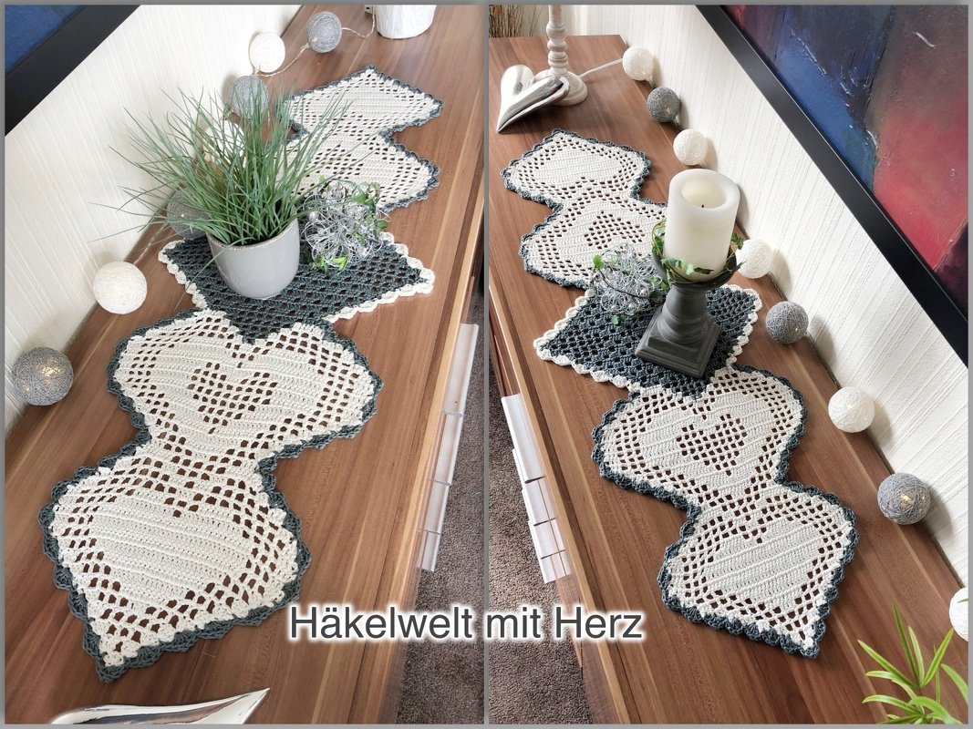 Gehäkelter Tischläufer aus verbundenen Herz- und Quadratmotiven in Creme mit grauem Rand auf einem Holzsideboard, dekoriert mit Kerze, Pflanze und Lichterkette.