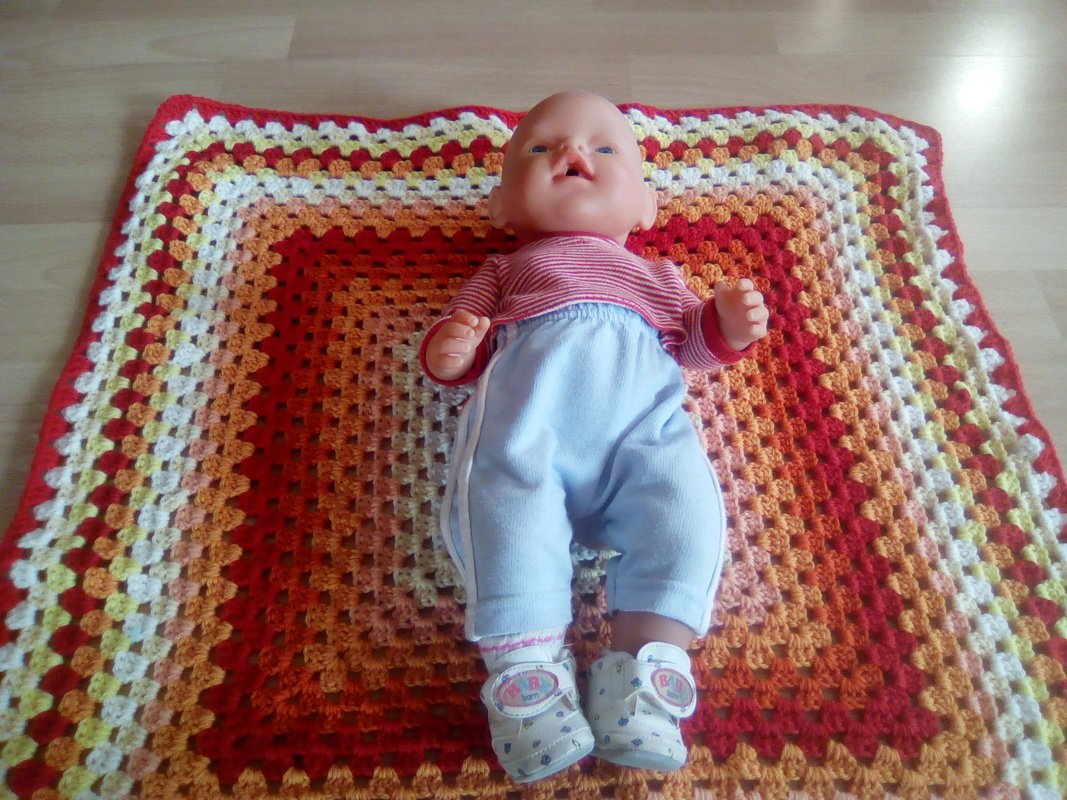 Gehäkelte Granny-Square-Babydecke in Rot, Orange, Gelb und Weiß mit einer Puppe