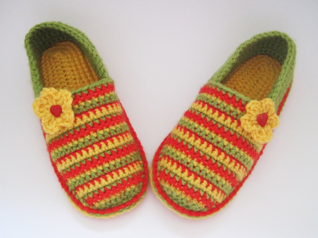 Paar gehäkelter Kinderschuhe in Rot, Gelb und Grün mit gelber Blumenapplikation