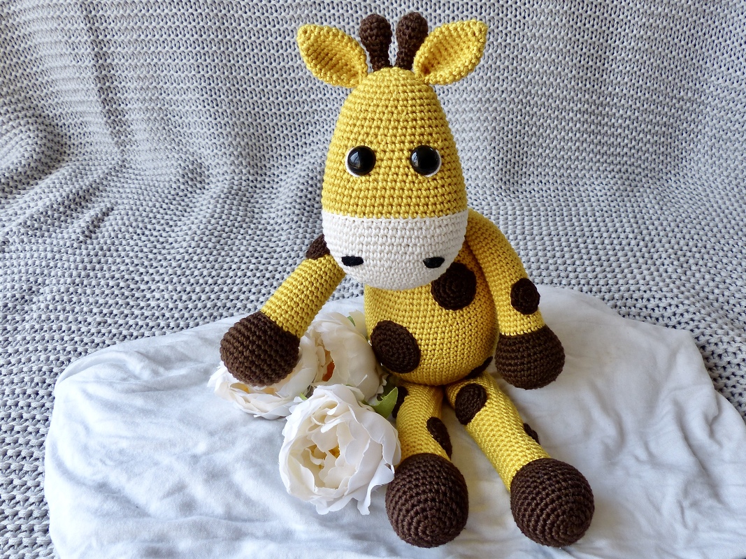 yellow crocheted giraffe toy with brown spots sitting on a knit blanket