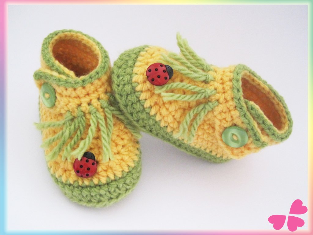 Gehäkelte gelb-grüne Babyschuhe mit Marienkäfer-Knöpfen und grünen Zierbändern auf hellem Hintergrund