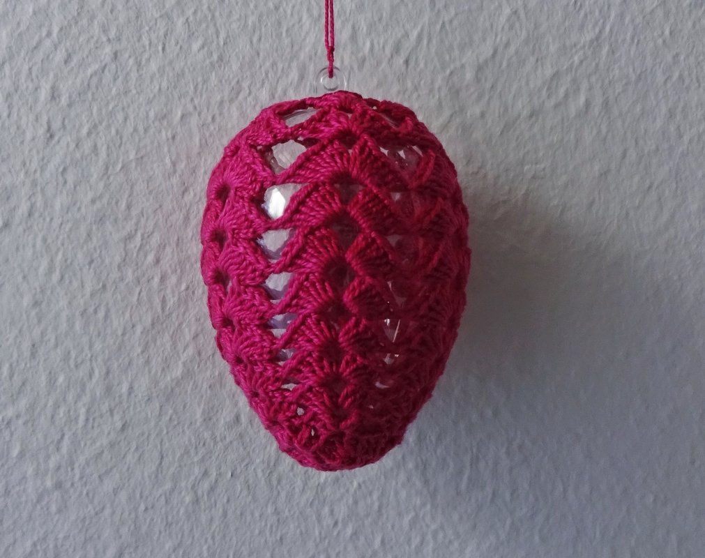 Nahaufnahme: pinke Häkelhülle mit Aufhänger um Osterei