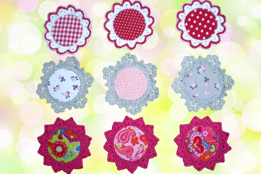 Neun runde, handgehäkelte Untersetzer mit gemusterten Stoffeinsätzen und gezackten Häkelrändern in Rot, Grau und Fuchsia.