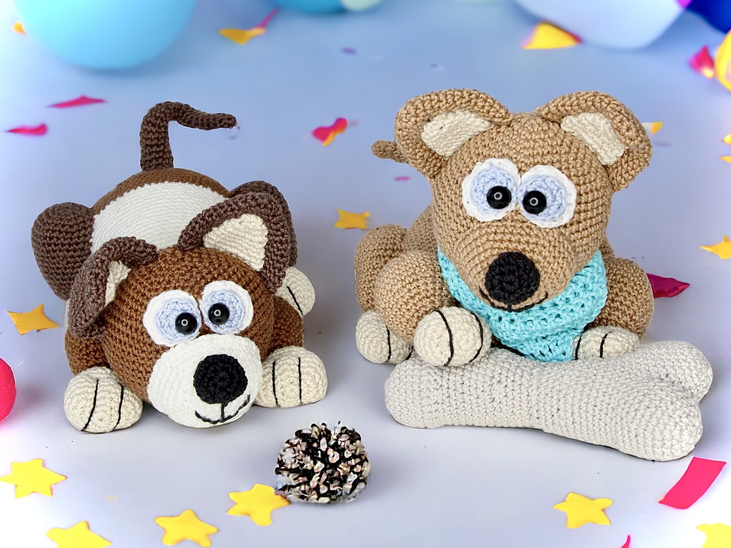 Close-up of two crocheted dog amigurumis showing ear shape, snouts, eyes and a crochet bone prop
