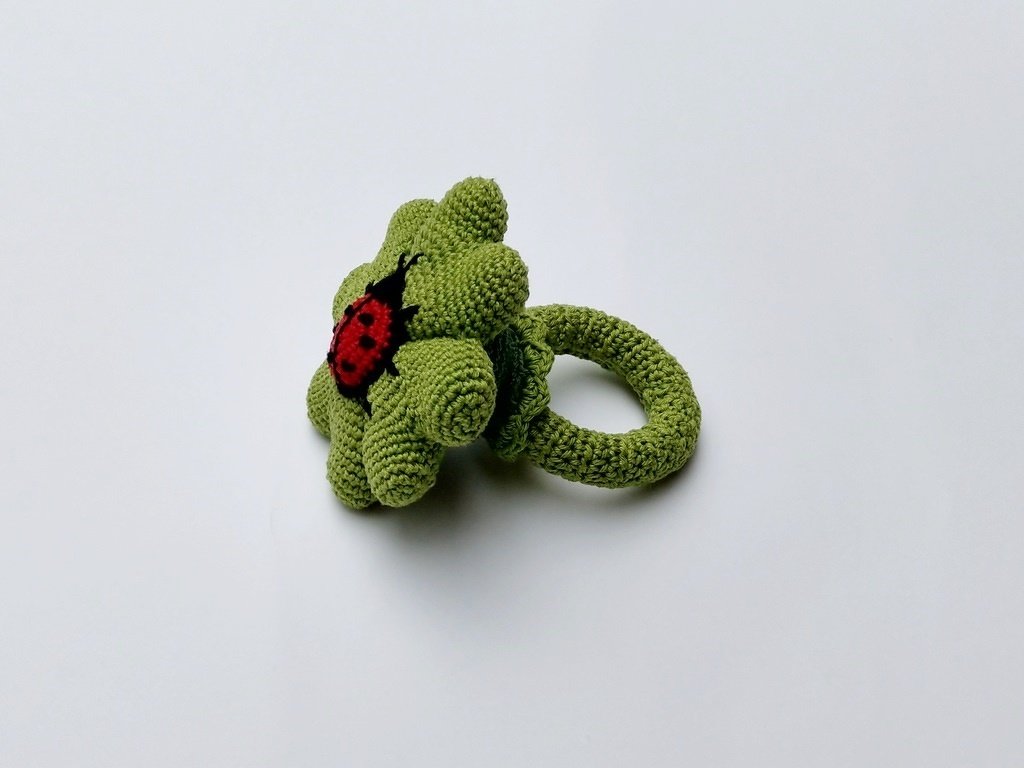 Gehäkelter grüner Blumen-Greifring mit rotem Marienkäfer in der Mitte, ideal für Babys