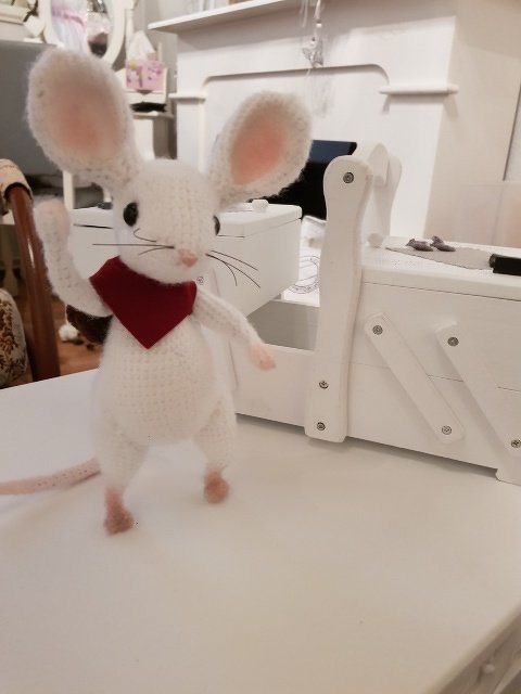 Weiße gehäkelte Amigurumi‑Maus mit rosa Ohren und rotem Halstuch auf hellem Untergrund