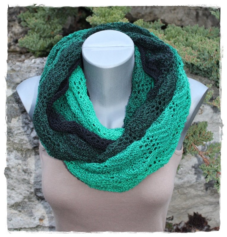 Gestrickter Loop-Schal in Grüntönen mit offenem Lochmuster auf Schaufensterpuppe vor steinig-grüner Kulisse