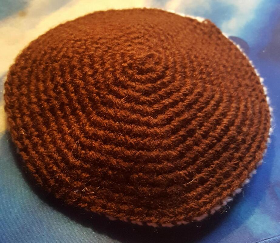 Nahaufnahme eines runden braunen Häkelkreises mit spiralförmigem Muster auf blauem Hintergrund