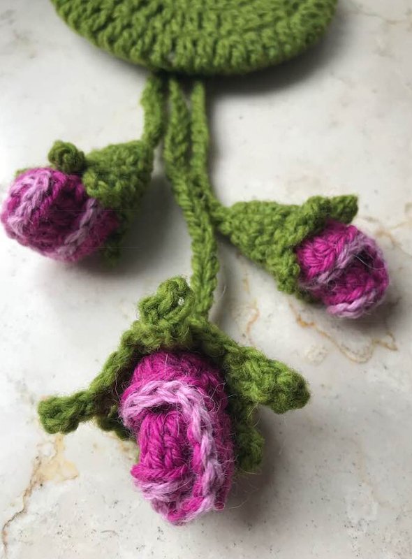 Nahaufnahme: drei gehäkelte Rosenknospen an grünen Stielen