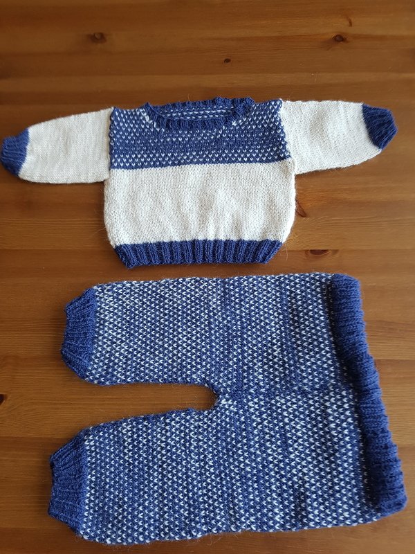 Blue and white hand-knitted baby sweater and matching pants laid flat on a wooden surface.