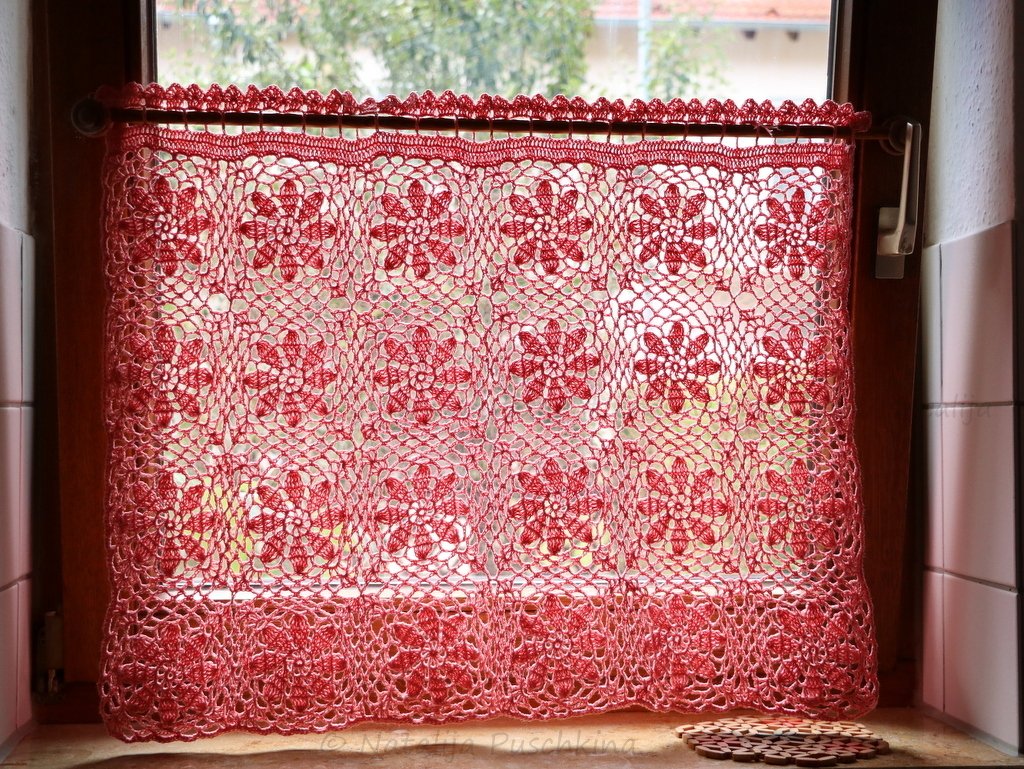 Rote gehäkelte Scheibengardine mit Blumenmotiven vor einem Fensterrahmen