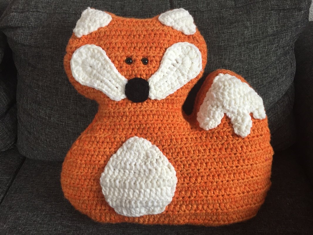 Gehäkeltes Fuchskissen in Orange, Weiß und Schwarz auf grauem Sofa