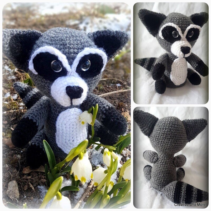 Gehäkelter Amigurumi-Waschbär mit schwarzer Augenmaske und geringeltem Schwanz zwischen Schneeglöckchen