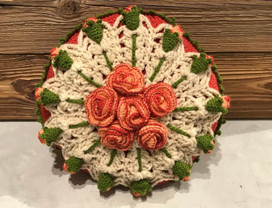 Nahaufnahme einer runden gehäkelten Kissenhülle mit orangefarbenen Rosen