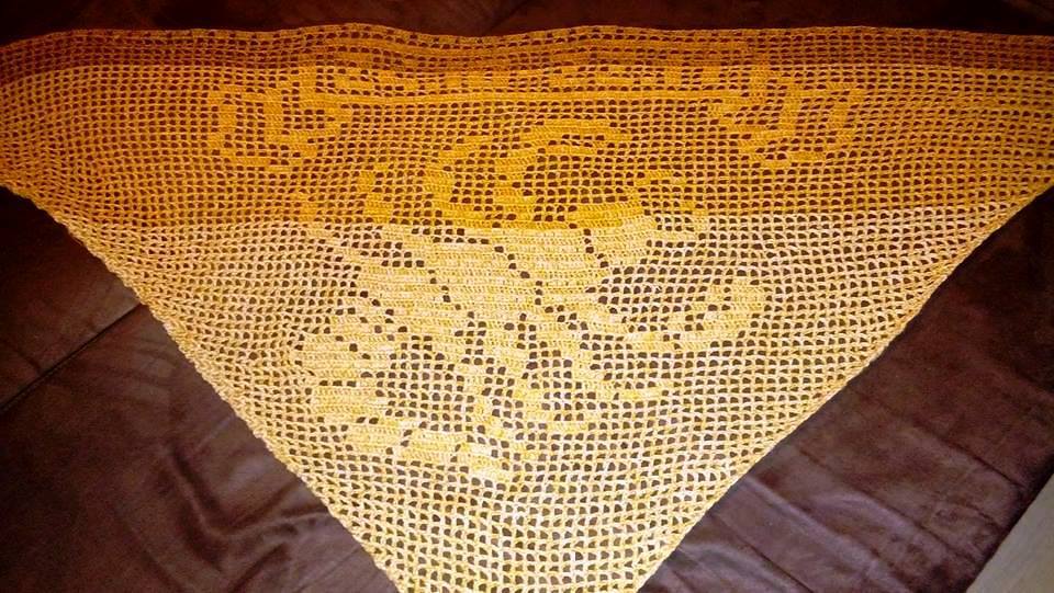 Dreieckiges, gehäkeltes Tuch in Gelb-Orange-Farbverlauf mit im Muster geformtem Schriftzug auf dunklem Untergrund