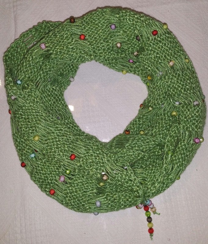 Grüner gestrickter Loop-Schal mit bunten Perlen auf hellem Untergrund
