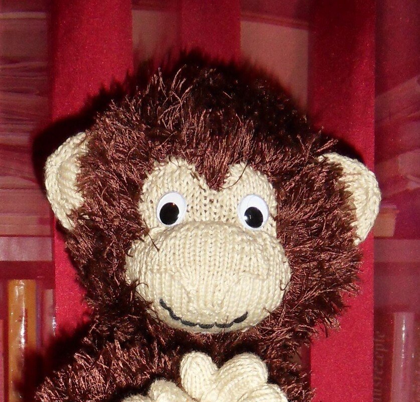 Nahaufnahme eines gestrickten Affen in Braun mit cremefarbenem Gesicht, flauschigem Garn und zusammengesetzten Pfoten