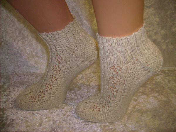 Helles Paar handgestrickter Damen-Kurzsocken mit Lochmuster und Rippenbund, an Füßen getragen.