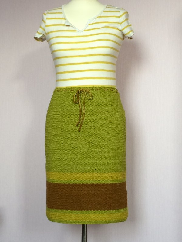 Knielanger gehäkelter Rock in Grün mit braunem und gelbgrünem Saumstreifen und Kordelzug, auf einer Schaufensterpuppe.