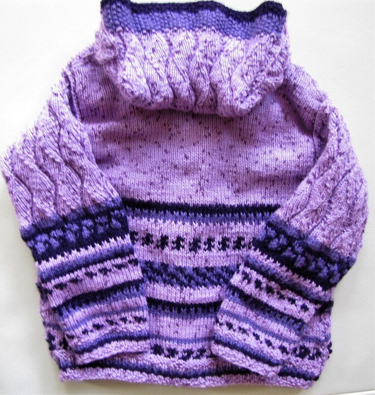 Gestrickter Pullover in verschiedenen Lilatönen mit Zopfmuster an den Ärmeln, hohem Kragen und gemusterten Streifen am Saum und an den Bündchen.